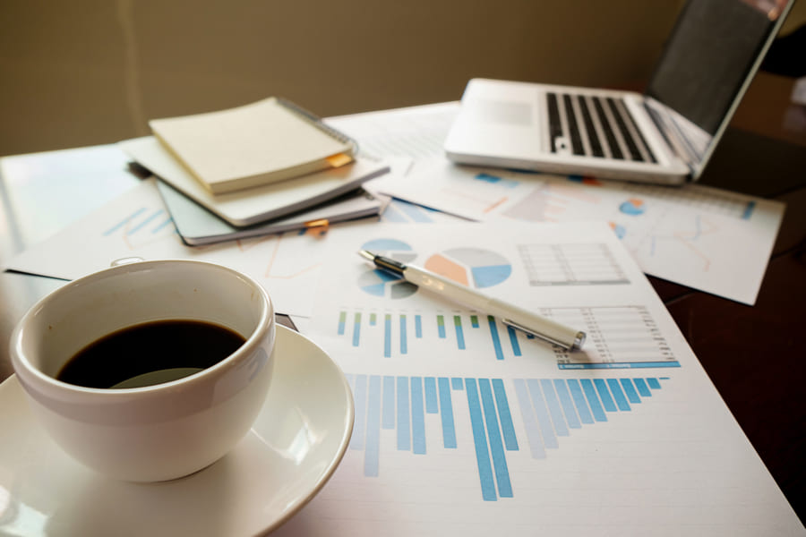 Coffee cup on a desk beside printed financial charts and a laptop.